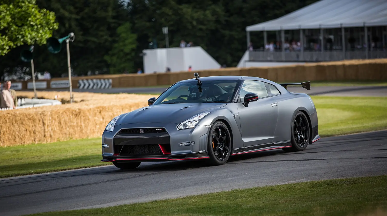 A grey supercar on the hill climb course at Goodwood Festival of Speed in 2014, hay bales and marquee behind