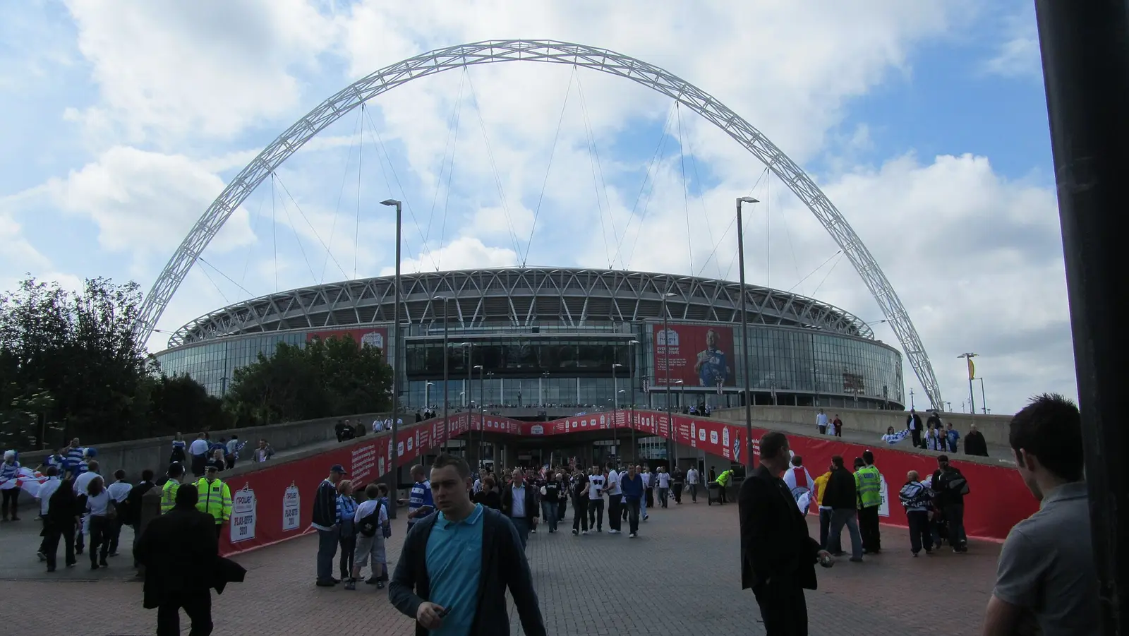 The Wembley arch over the stadium with fans walking up Wembley Way on a match day